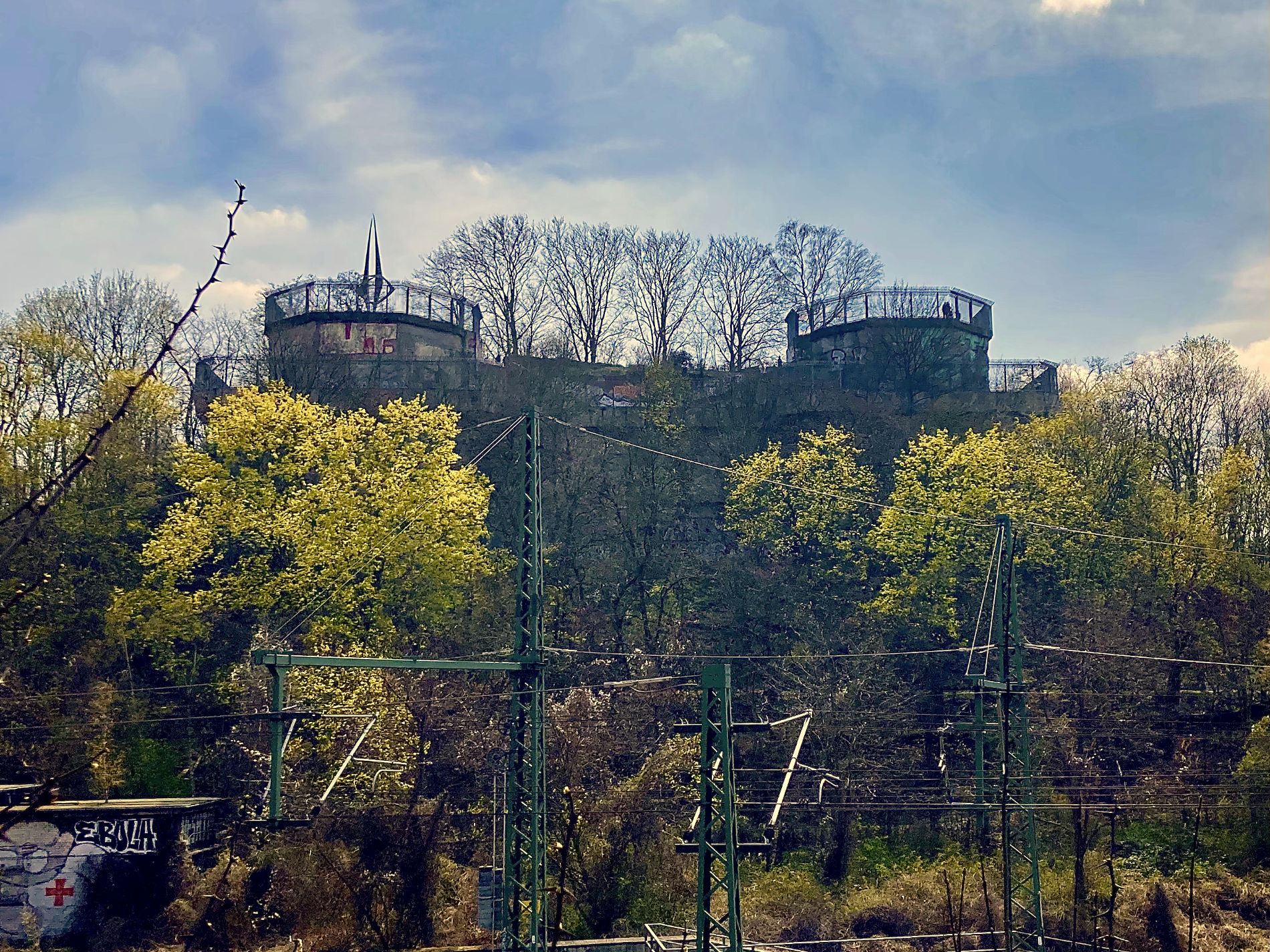 The flak tower rises above the trees next to the railroad.